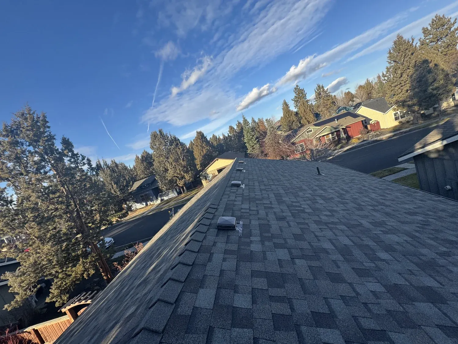 Newly finished dark shingle roof and ridge under a blue sky